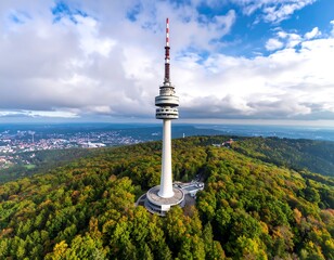 Obraz premium Aerial view of a tall, slender tower atop a forested hill, overlooking a sprawling city under a partly cloudy sky