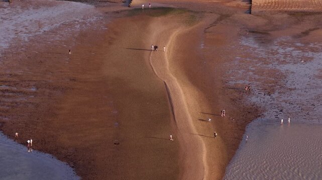 People walking on a serene Whitstable beach at sunset in Kent, UK