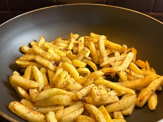 Golden crispy French fries frying in a pan with spices on a home kitchen. Closeup of delicious potato cooking process, rustic homemade comfort food.