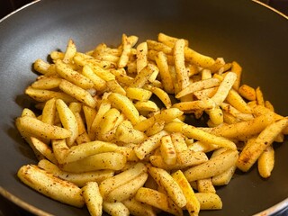Crispy homemade French fries with spices cooking in a frying pan. Close-up view of golden potato slices prepared at home. Comfort food, tasty snack, rustic style.