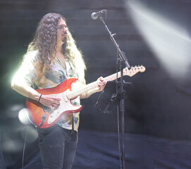 Guitarist performing live music on stage, playing electric guitar under bright spotlights