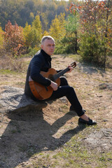 Portrait of smiling caucasian artist plays wooden acoustic guitar in autumnal park. Young songwriter plays string musical instrument hobby outside in nature fall time. Audio music healing in natural