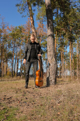 Blonde man playing string guitar outdoors in autumn forest. Concept of sound therapy, mental health...