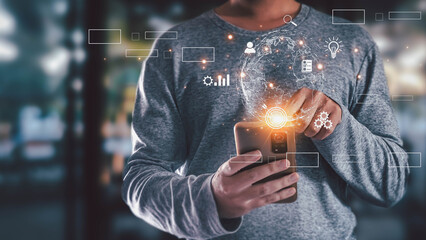 Man using smartphone with holographic globe and business icons. Concept of global technology, digital transformation, network connection, and innovative ideas.
