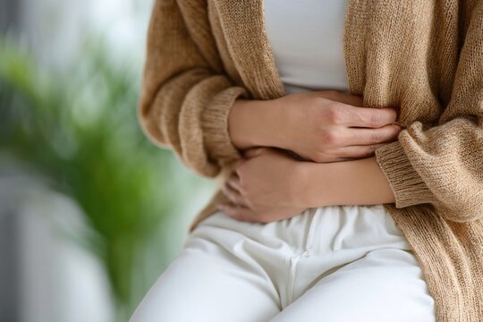 Close up of woman experiencing stomach or abdominal pain, holding her belly with hands, concept of health care and medical
