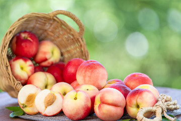 Fresh peach drop from bamboo basket on blurred greenery background, Peach fruit in Bamboo basket on wooden table in garden.