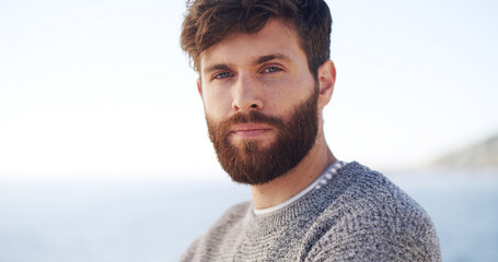 Portrait, travel and man at ocean for vacation, summer trip or adventure with space. Beach, tourist and serious person at outdoor with confidence on holiday at sea on tropical island in Greece