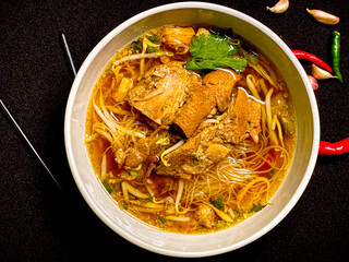 Braised duck noodle soup served in a bowl with fresh herbs and green onions. Tender duck with rich,...