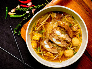 Braised pork noodle soup served in a bowl with fresh herbs, green onions, and chili. Traditional...