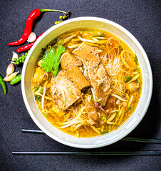 Braised duck noodle soup served in a bowl with fresh herbs and green onions. Tender duck with rich,...