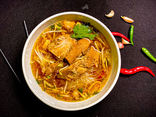 Braised duck noodle soup served in a bowl with fresh herbs and green onions. Tender duck with rich,...
