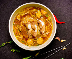 Braised pork noodle soup served in a bowl with fresh herbs, green onions, and chili. Traditional...