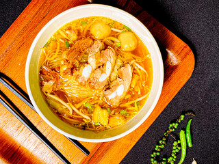 Braised pork noodle soup served in a bowl with fresh herbs, green onions, and chili. Traditional...