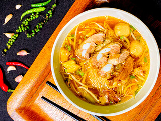 Braised pork noodle soup served in a bowl with fresh herbs, green onions, and chili. Traditional...