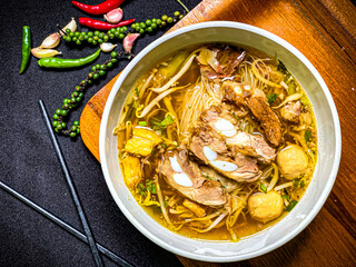Braised pork noodle soup served in a bowl with fresh herbs, green onions, and chili. Traditional...