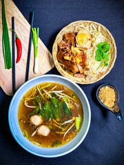 Thai braised pork leg noodle soup served in a bowl with fresh herbs, boiled egg, and green onions. Tender pork leg and rich savory broth with soft noodles, a traditional and appetizing Thai comfort fo
