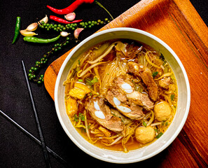 Braised pork noodle soup served in a bowl with fresh herbs, green onions, and chili. Traditional...