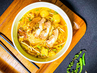 Braised pork noodle soup served in a bowl with fresh herbs, green onions, and chili. Traditional...