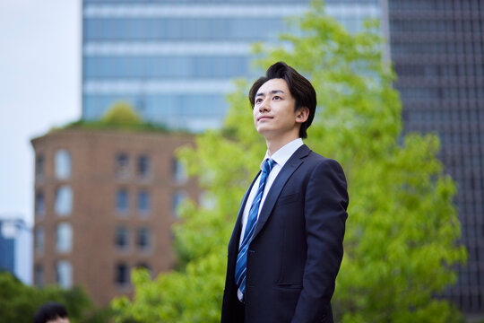 ビルを背景に遠くを見つめるスーツを着た日本人ビジネスマンの男性