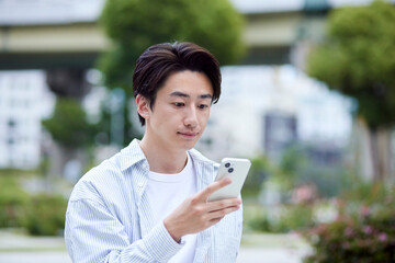休日の公園でリラックスしてスマートフォンを操作する私服の日本人男性