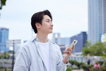 休日の公園でリラックスしてスマートフォンを操作する私服の日本人男性
