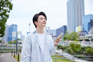 休日の公園でリラックスしてスマートフォンを操作する私服の日本人男性