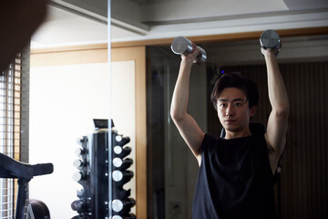 フィットネスジムで筋力トレーニングを行うスポーツウェアを着た若い日本人男性