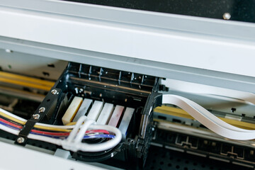 Close-up view of a professional inkjet printer during maintenance process, showing ink cartridges, printhead and ribbon cable inside industrial printing equipment