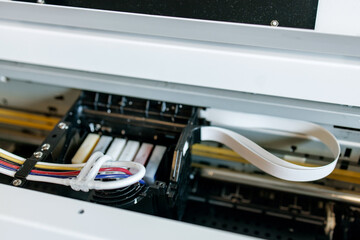 Close-up view of a professional inkjet printer during maintenance process, showing ink cartridges, printhead and ribbon cable inside industrial printing equipment