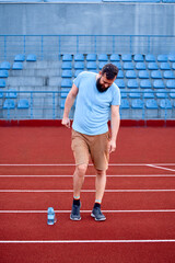 Obraz premium A man is taking a break on a red track field, with a water bottle nearby, showcasing a moment of relaxation and hydration after athletic or casual exercise in an outdoor setting.