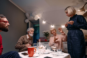 A group of people enjoying conversation while seated at a dining table in a cozy room decorated with festive lights and balloons.