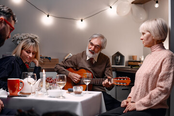 Family members gather around a table, enjoying a heartfelt moment with music and conversation.