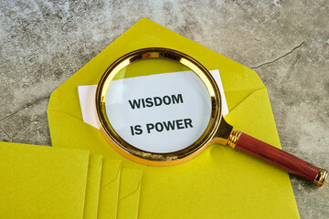 A magnifying glass highlights the text Wisdom is power on a piece of paper within a yellow...