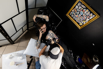 Tattooed man talking on the phone while getting a tattoo in a professional studio. A candid moment capturing multitasking, casual mood, and modern lifestyle in a creative space