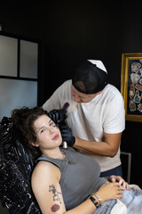 Smiling tattoo artist prepares for the session while a young woman relaxes in the chair, moments...