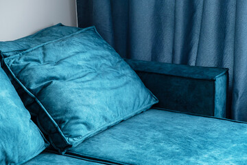 Close up of teal blue couch with fluffy pillows and matching curtains in cozy living room.