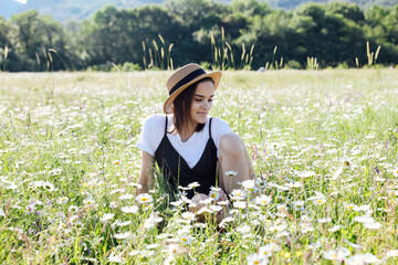 woman in dress and hat on a field of daisy flowers