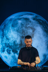 DJ Performing Live with Artistic Moon Backdrop Under Subdued Lighting