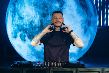 DJ Performing on Stage With Headphones and Blue Planet Background