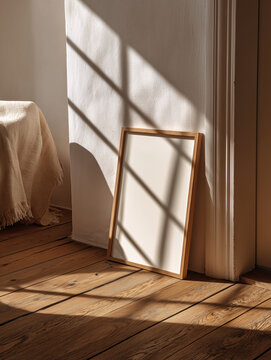 A thin light wooden picture frame leaning against the wall on the floor with a white background