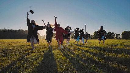 Happy graduates celebrating at sunset, tossing their caps and diplomas in the air as they run...