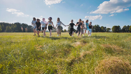 Group of high school students enjoying summer break, running together across a grassy field, holding hands, and having fun