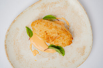 A crafted croquette on a textured plate, paired with creamy sauce and leaves, showcases artistry
