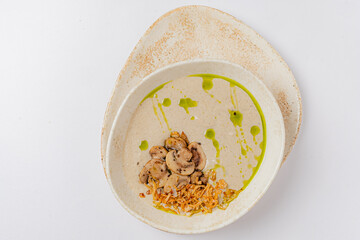 A delicate bowl features creamy mushroom slices adorned with vibrant green oil and crispy bits