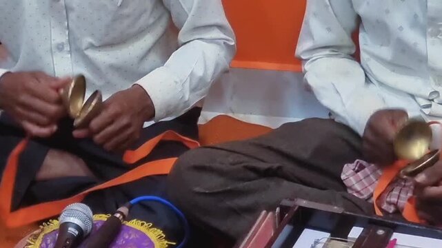 Two people playing Manjira (hand cymbals) during a Hindu ritual, potentially a Ganesh Chaturthi pooja. Manjira are integral to devotional music, enhancing prayers and creating a spiritual ambiance