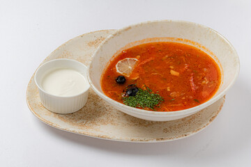 Delicious tomato-based soup garnished with herbs and lemon, accompanied by a creamy white sauce