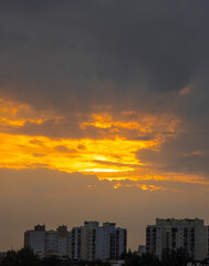Fototapeta premium An intensely orange sunset piercing through thick storm clouds over the city skyline