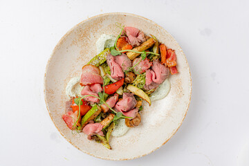 Tender cuts of beef atop a colorful mix of roasted vegetables, paired with a creamy dressing