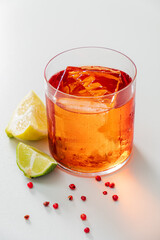 A vibrant cocktail in a crystal glass, garnished with lime and pink peppercorns, awaits
