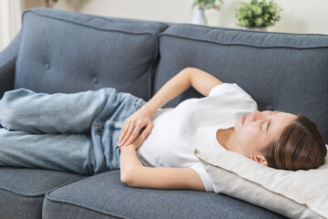 Sick asian young woman in pain, hand holding belly, stomach pain from food poisoning, girl hurt...